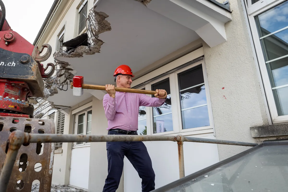 Man sieht einen Mann mit einem roten Helm, der mit beiden Händen einen Abbruchhammer im Anschlag hält.
